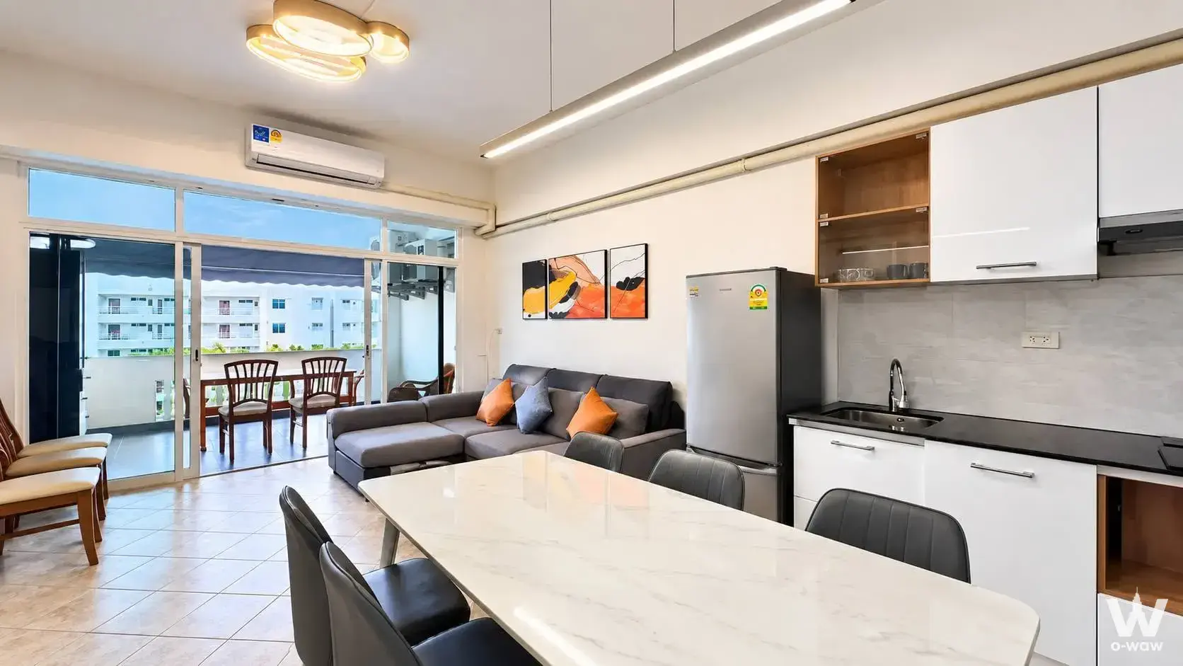 The open-plan living, dining and kitchen in a 1-bed Jomtien condo for rent has a grey sectional and balcony access