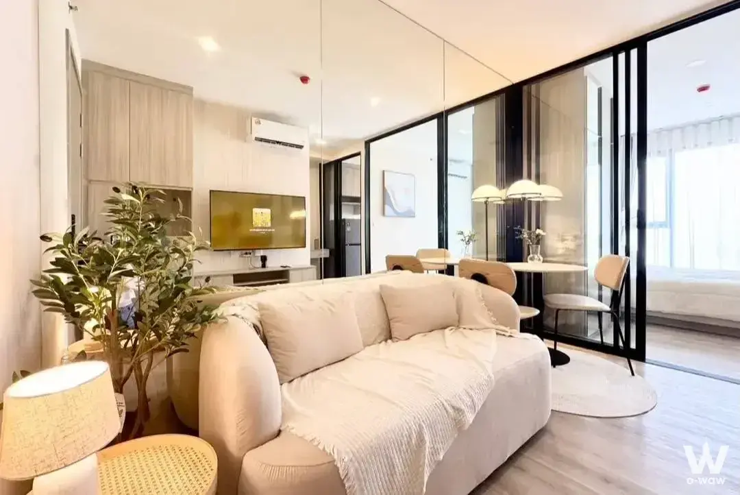 Living room in a 1-bed Origin Place Bangna condo has a cream sofa, glass partition and dining area
