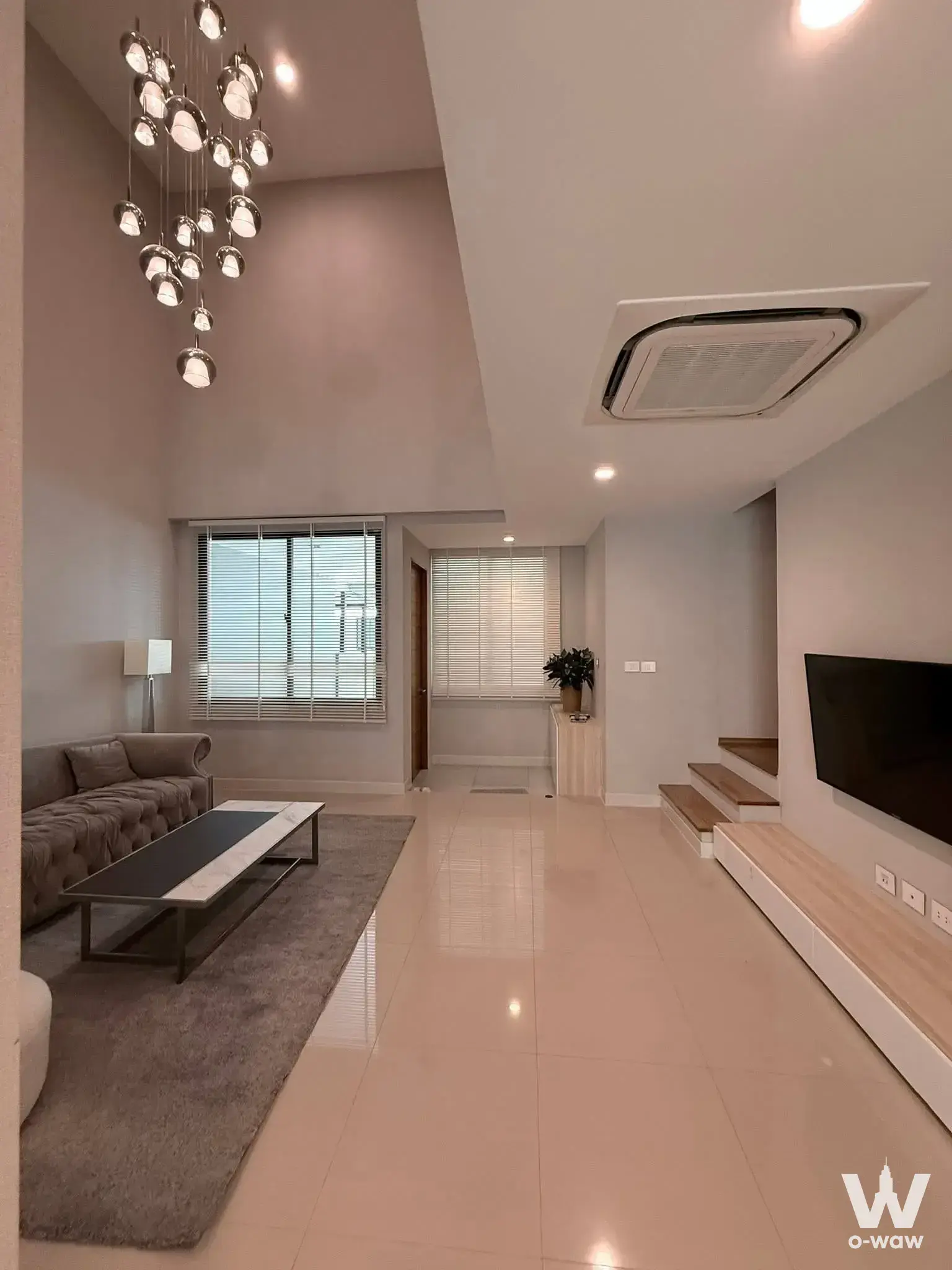Spacious living room with grey sofa, marble coffee table, and pendant lights in 3-bed townhouse for rent Nirvana Define Rama