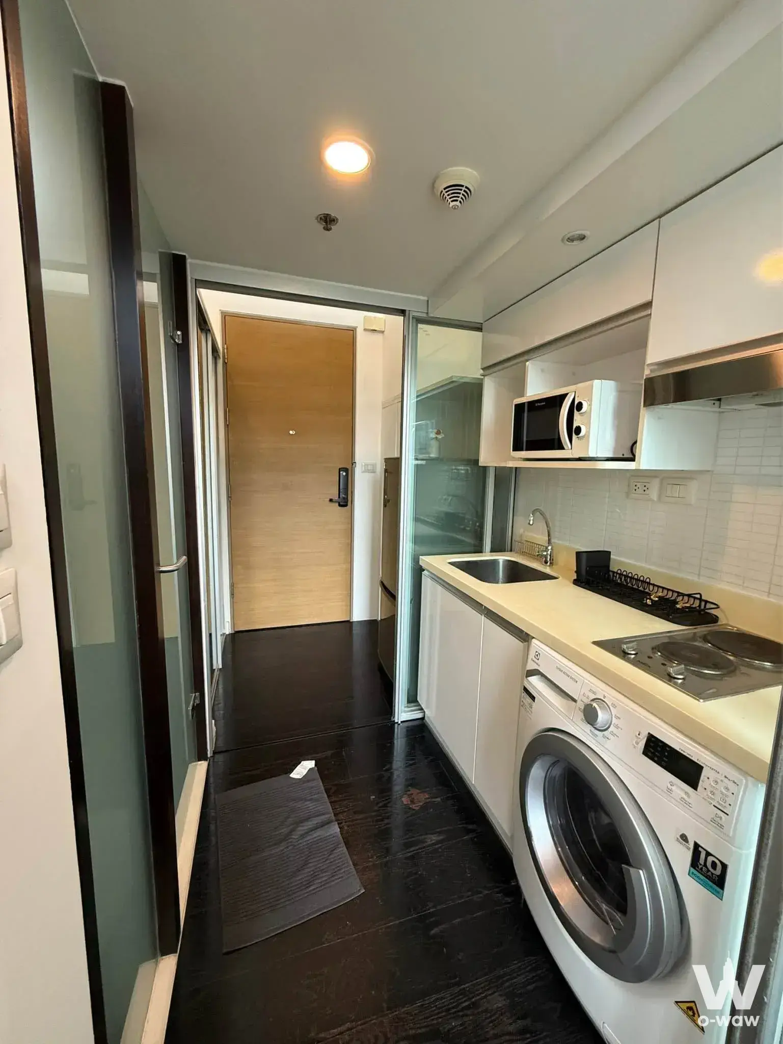 Compact kitchenette in a 1-bed condo for rent in Ideo Morph 38 with white cabinets and a washing machine
