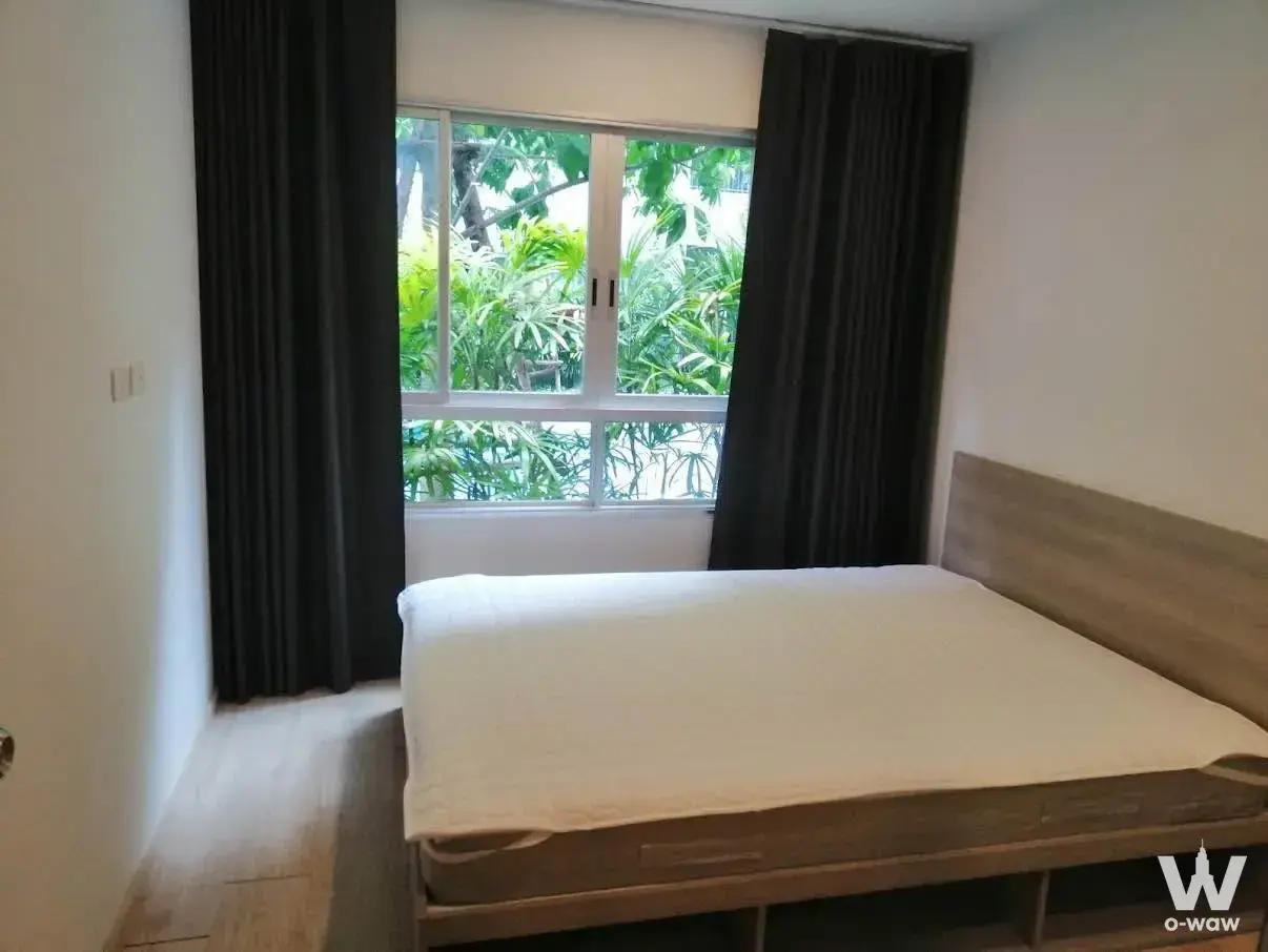 Minimalist bedroom with oak bed frame and garden view in Elio Del Moss condo