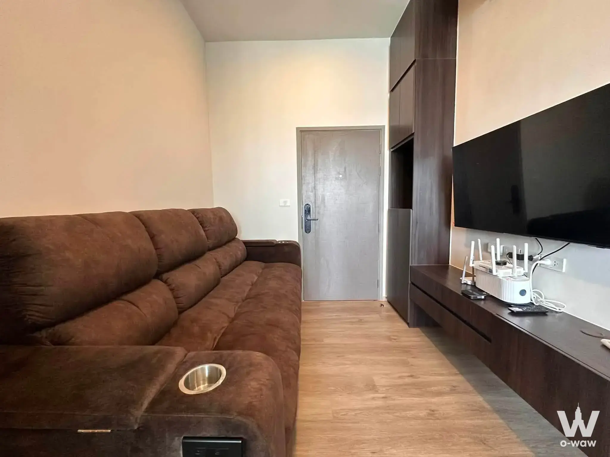 Living room in The Origin Plug & Play Ramintra with brown sofa, dark walnut media unit, and wall-mounted TV