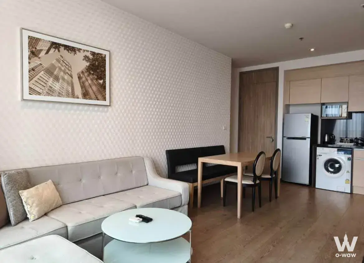 Open-plan living and dining area in a Park Origin Phrom Phong condo with light oak floors and a compact kitchenette