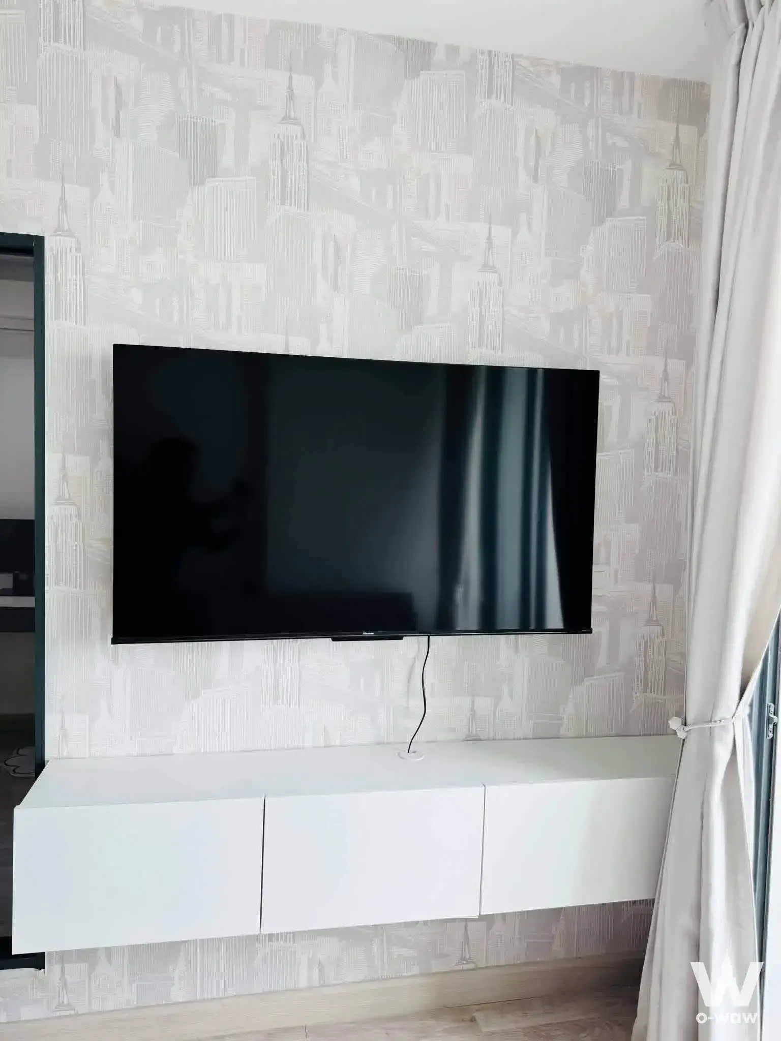 Black TV on grey skyline wallpaper above white console in a 1-bed unit for rent at Ideo Mobi Sathorn