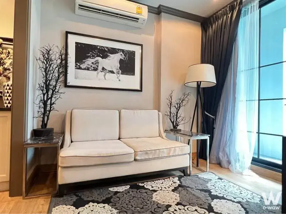 Living room in The Reserve Kasemsan 3 condo with cream leather sofa, damask rug, and black-and-white horse art