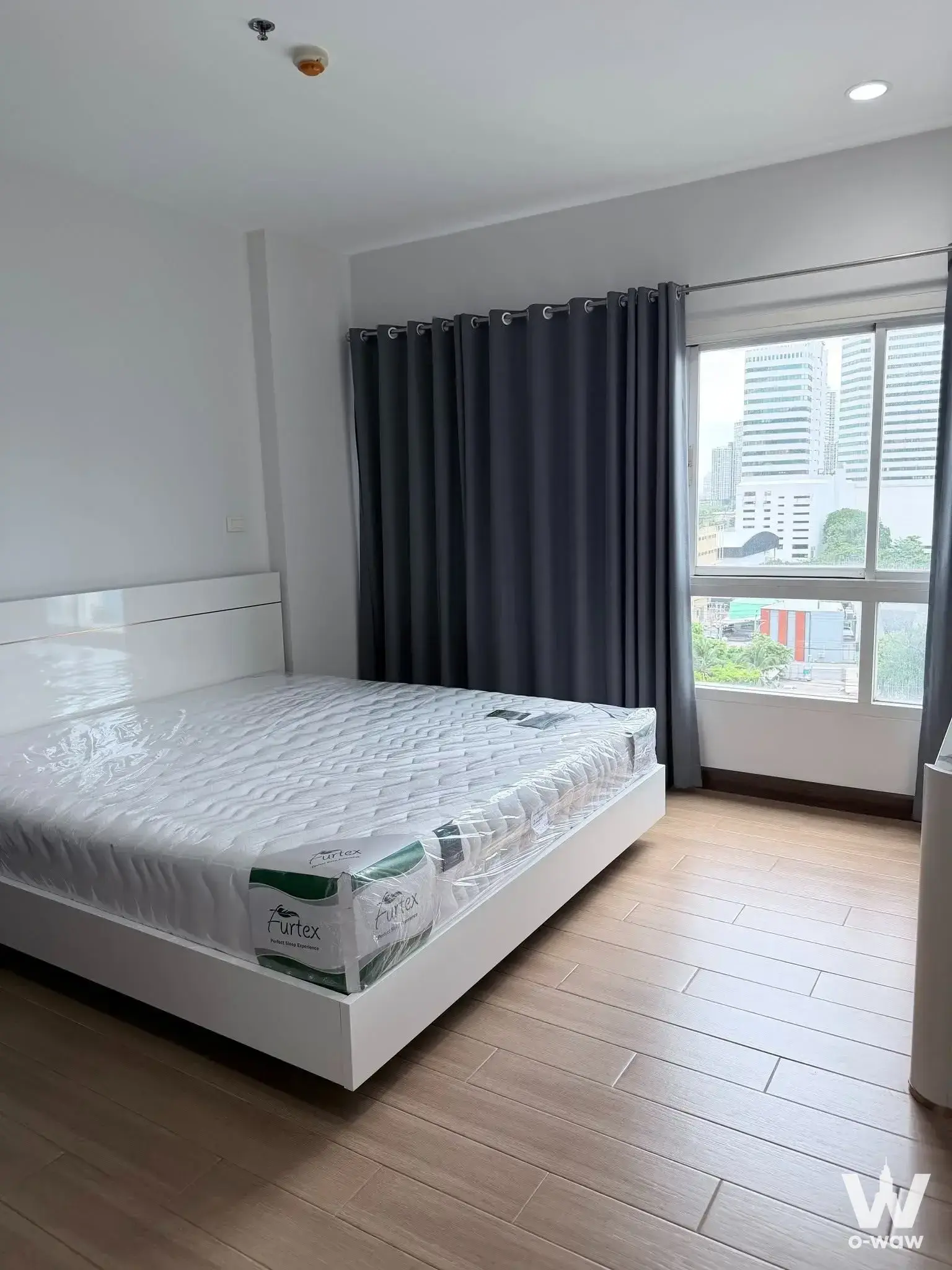 Unfurnished bedroom with white bed frame and large window in 1-bed condo for rent at PG Rama 9