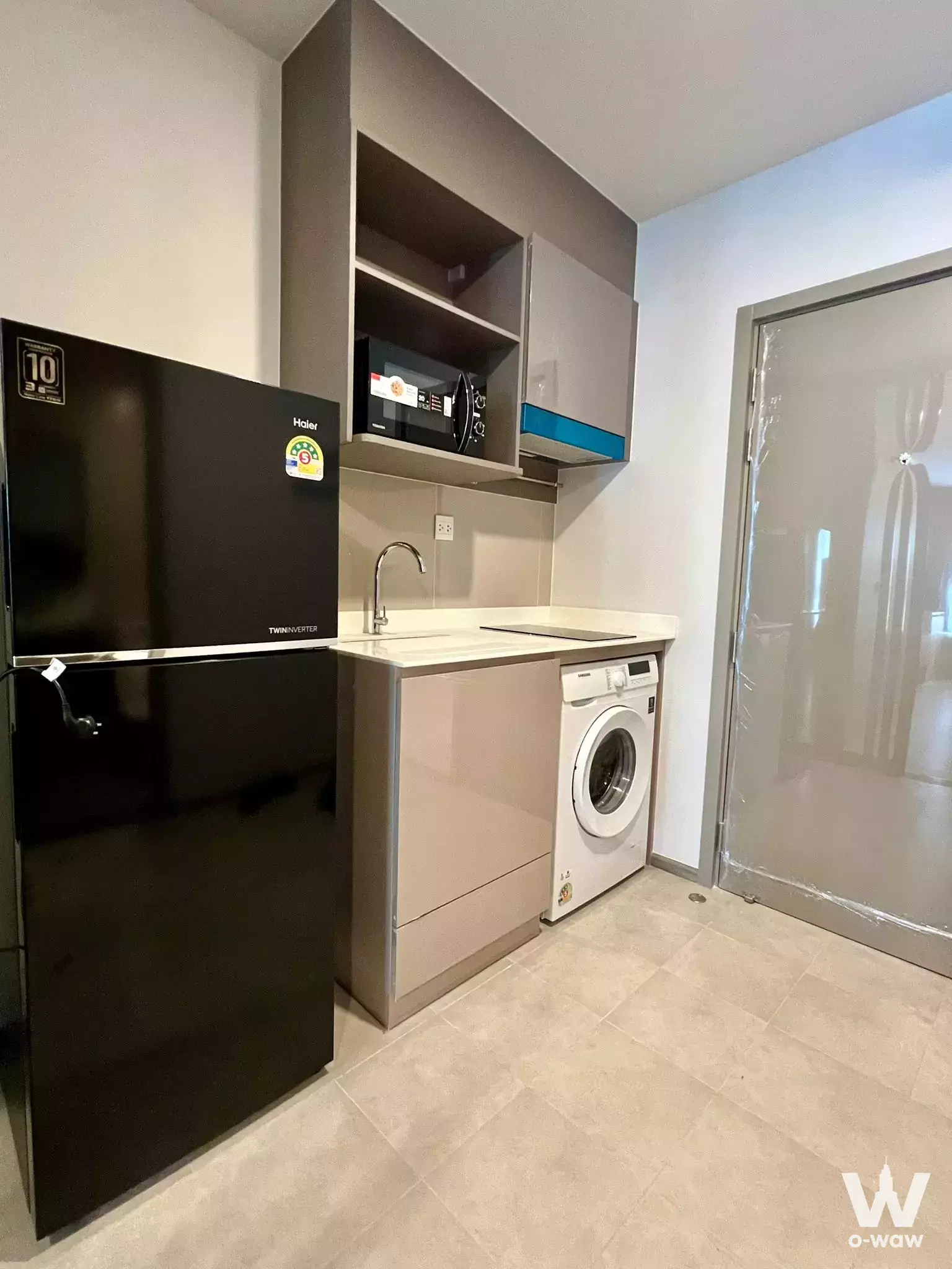 Compact kitchenette in Aspire Sukhumvit-Rama 4 with taupe cabinets, black fridge, and washing machine