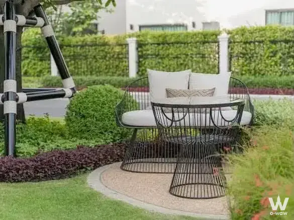 Black wire-frame garden seating on a pebble patio in this 4-bed house for sale at Setthasiri Bangna KM.10