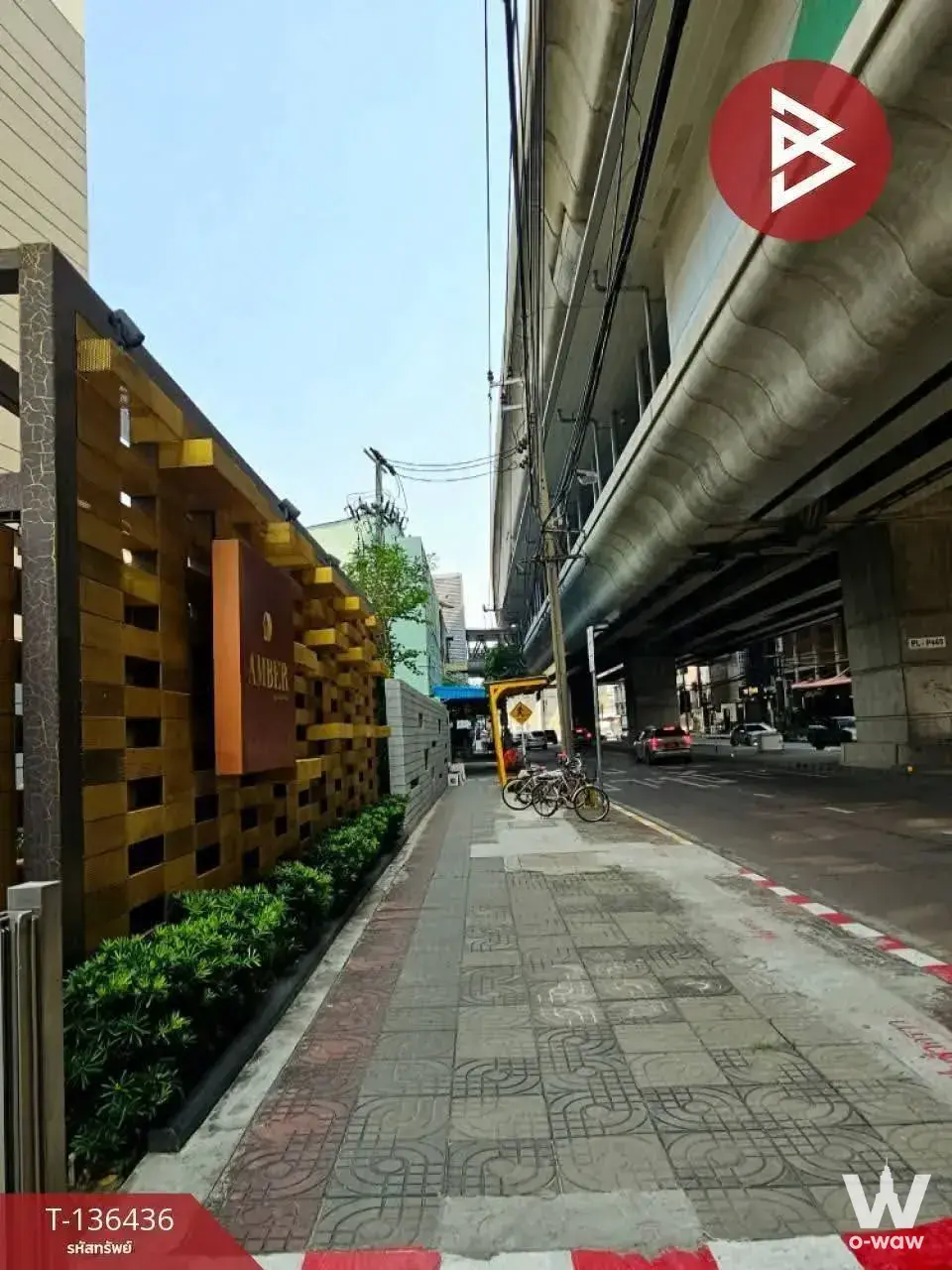 Amber Condominium entrance facade with golden-brown wooden block grid pattern beside elevated railway pillars