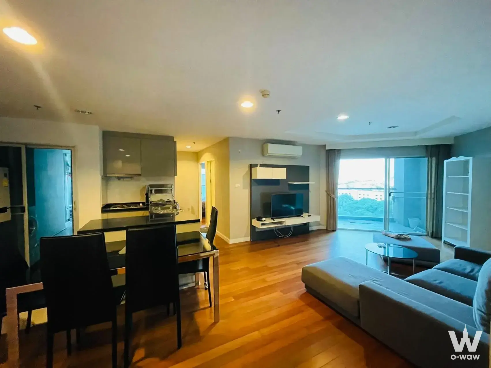 Open-plan living and dining area with grey sectional sofa, black dining set, and open kitchen with city views