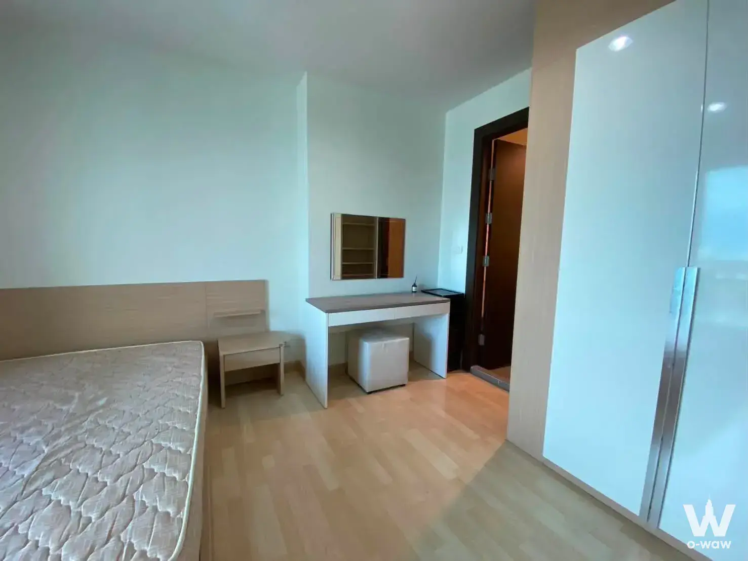 Minimalist bedroom in RHYTHM Ratchada featuring light wood flooring, white sliding wardrobe doors, and a built-in desk