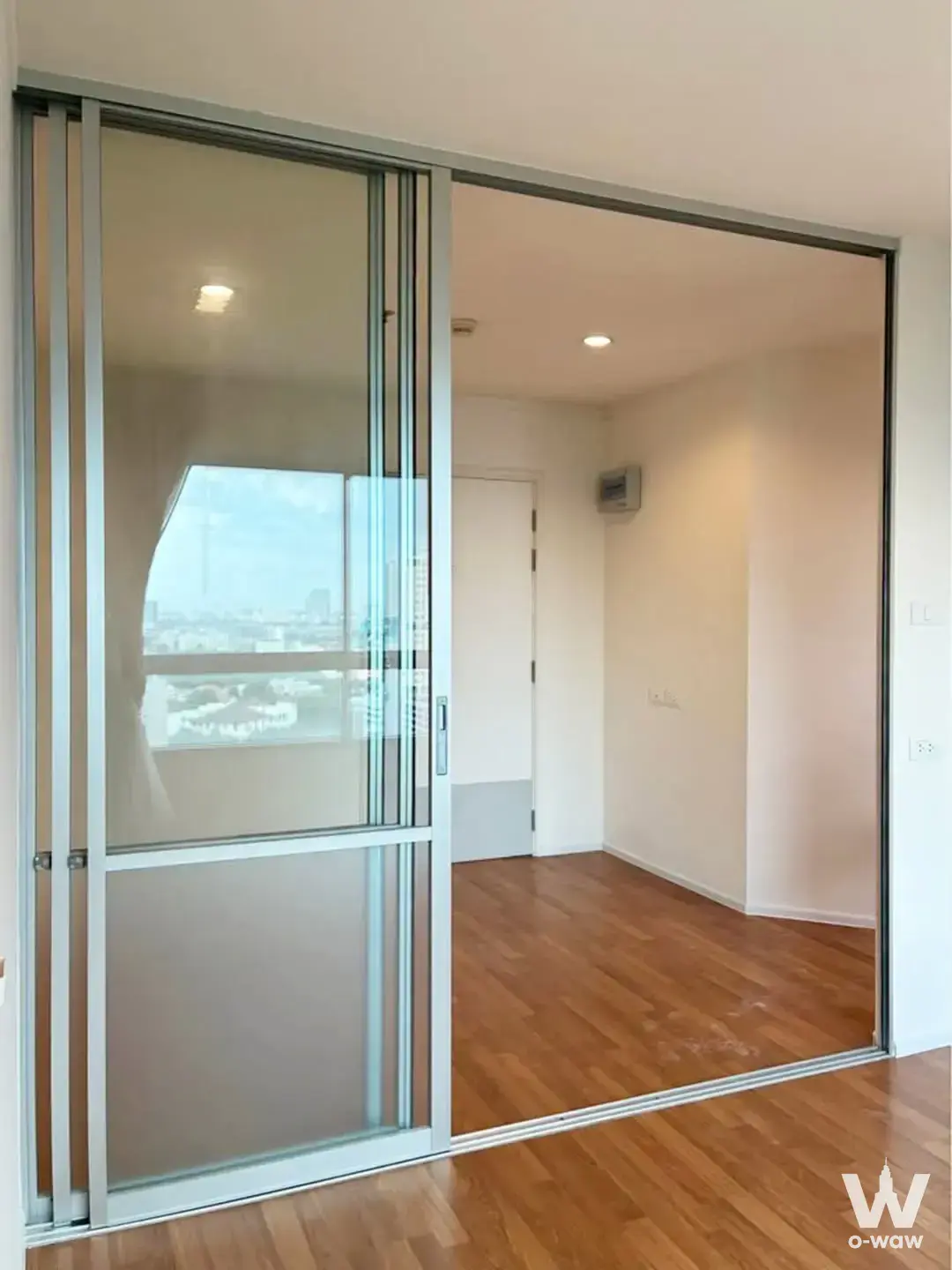 Empty bedroom in Lumpini Park Rama 9 with laminate floors and a sliding glass partition showing city views