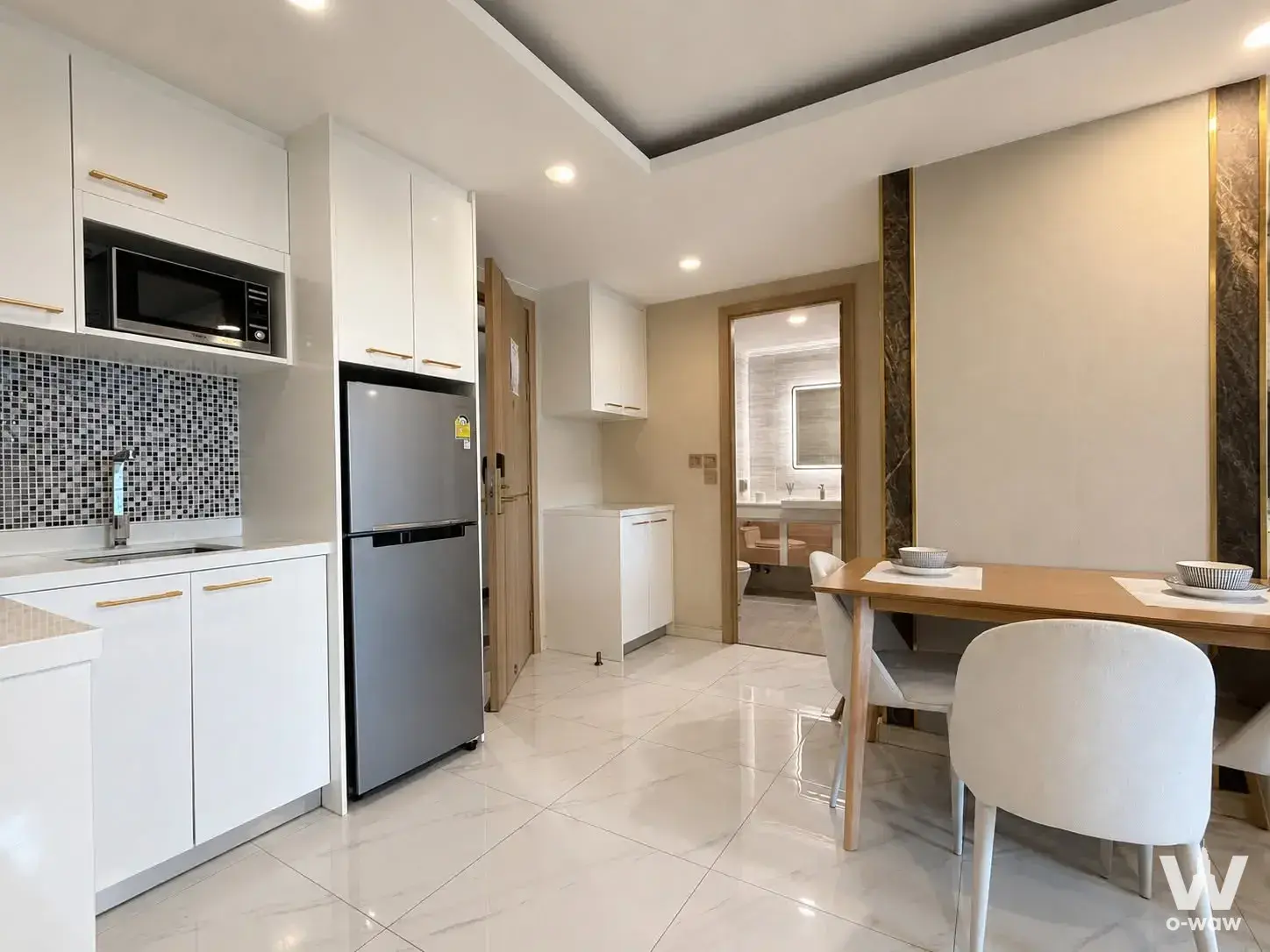 Modern open-plan kitchen and dining area with white marble floors, sleek cabinetry, and a wooden table set for two