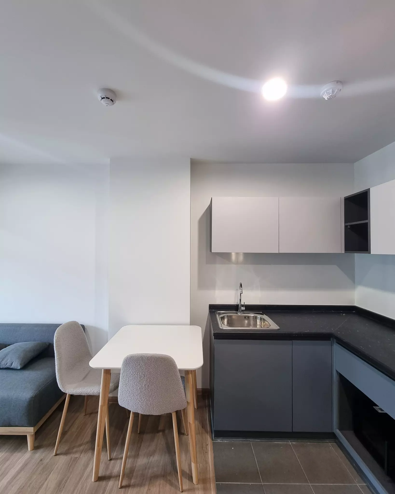 Studio living area in ARLO Sukhumvit 105 with blue-grey sofa, dining set, and open-plan grey and white kitchen