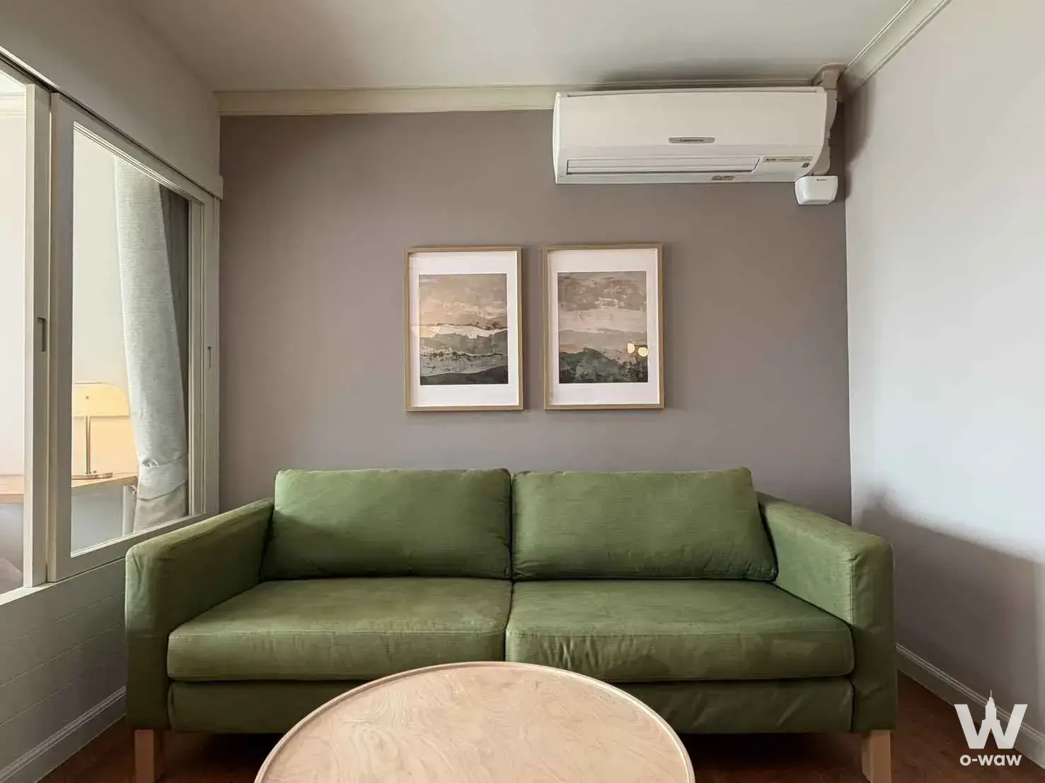 Minimalist living room with sage-green sofa against taupe accent wall and hardwood floors