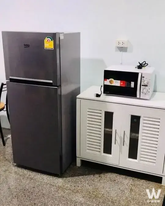 Functional kitchen corner in Sathorn House 2-bed condo showing fridge, louvered cabinet, and microwave