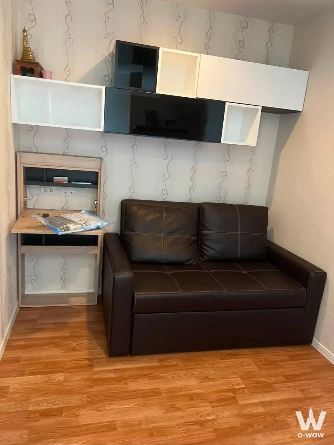 Compact living area featuring a brown leather sofa and floating storage units in a Lumpini condo