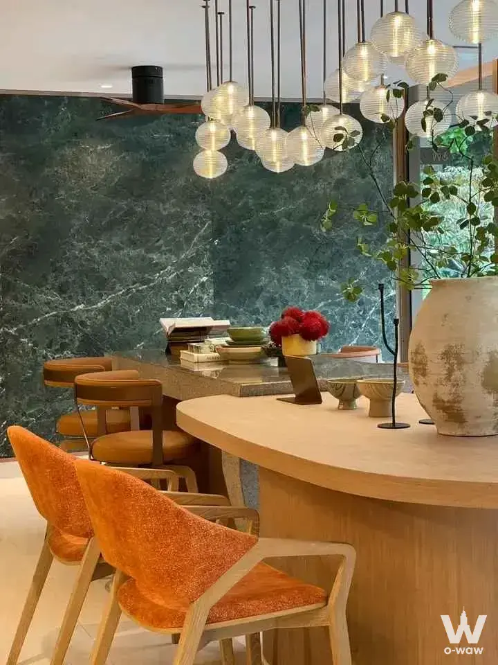 Luxury Mekin Haus condo dining area featuring dark green marble wall, curved table, and orange armchairs