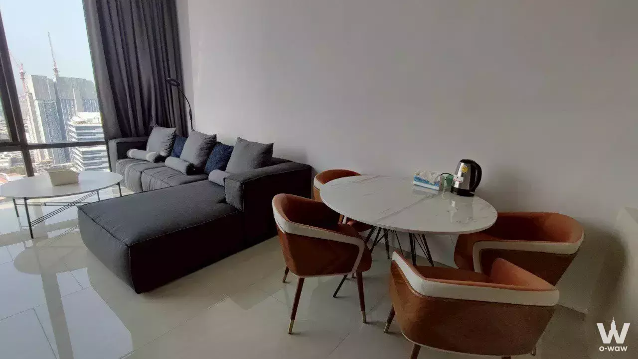 Living and dining area in Ashton Silom with grey sectional, marble table, and city views