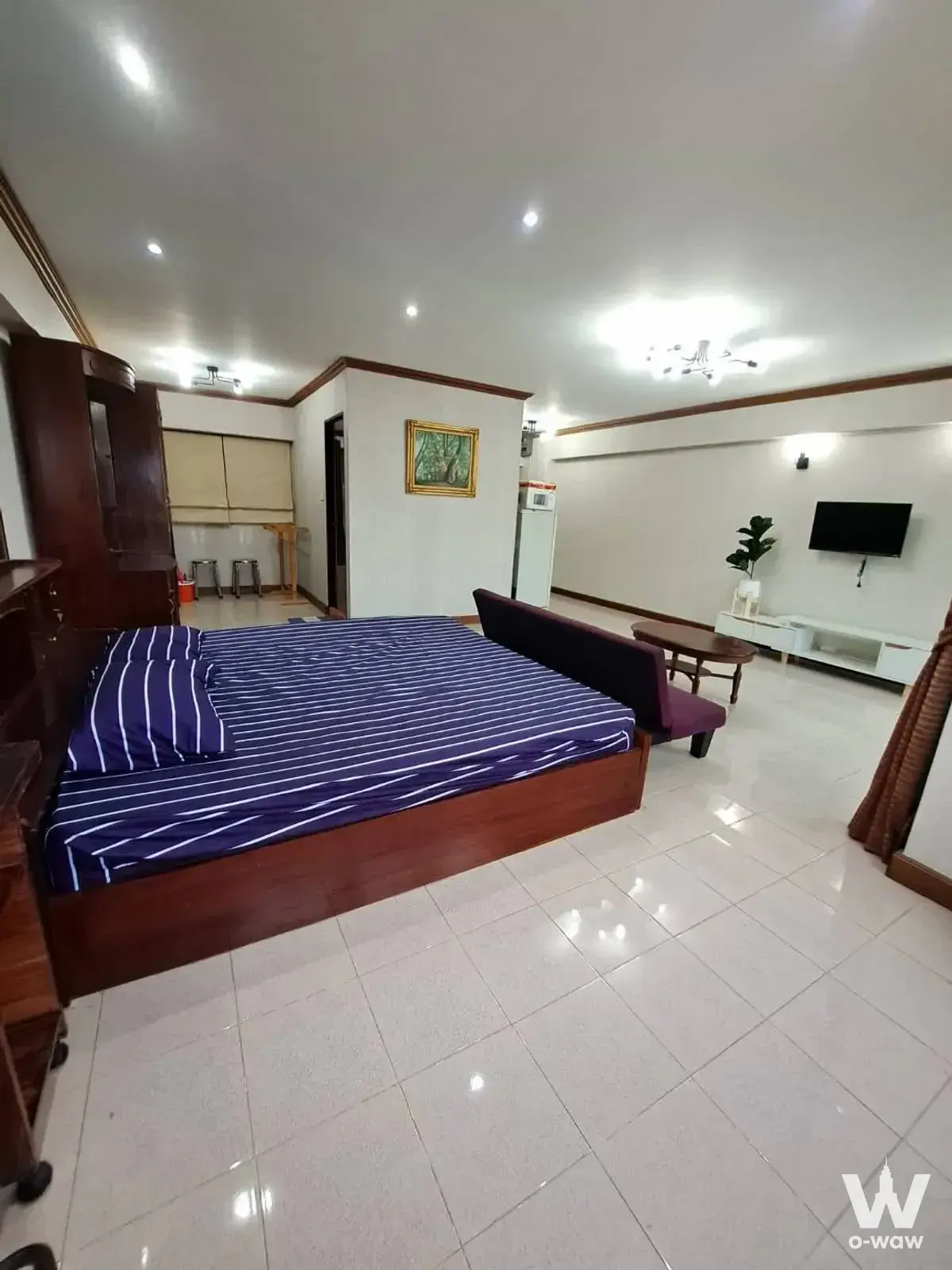 1-bed Park Thonglor Tower condo room with dark wood bed, TV console, and open kitchenette