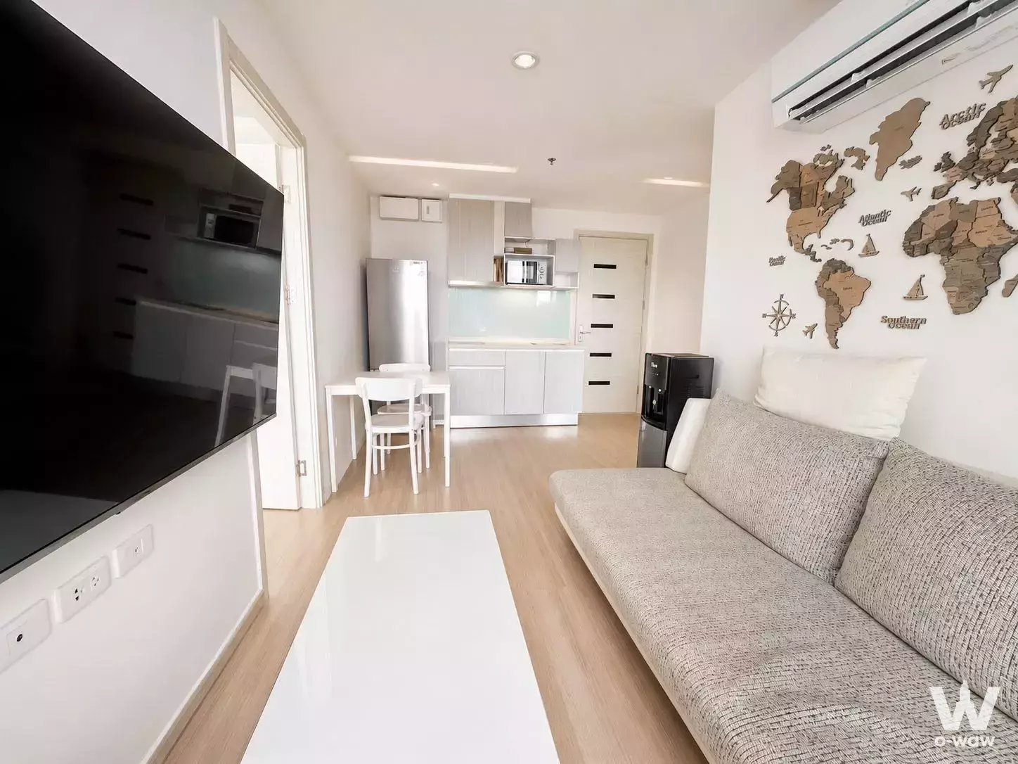 Living area in Artemis Sukhumvit 77 condo with beige sofa, world map wall art, and compact dining set