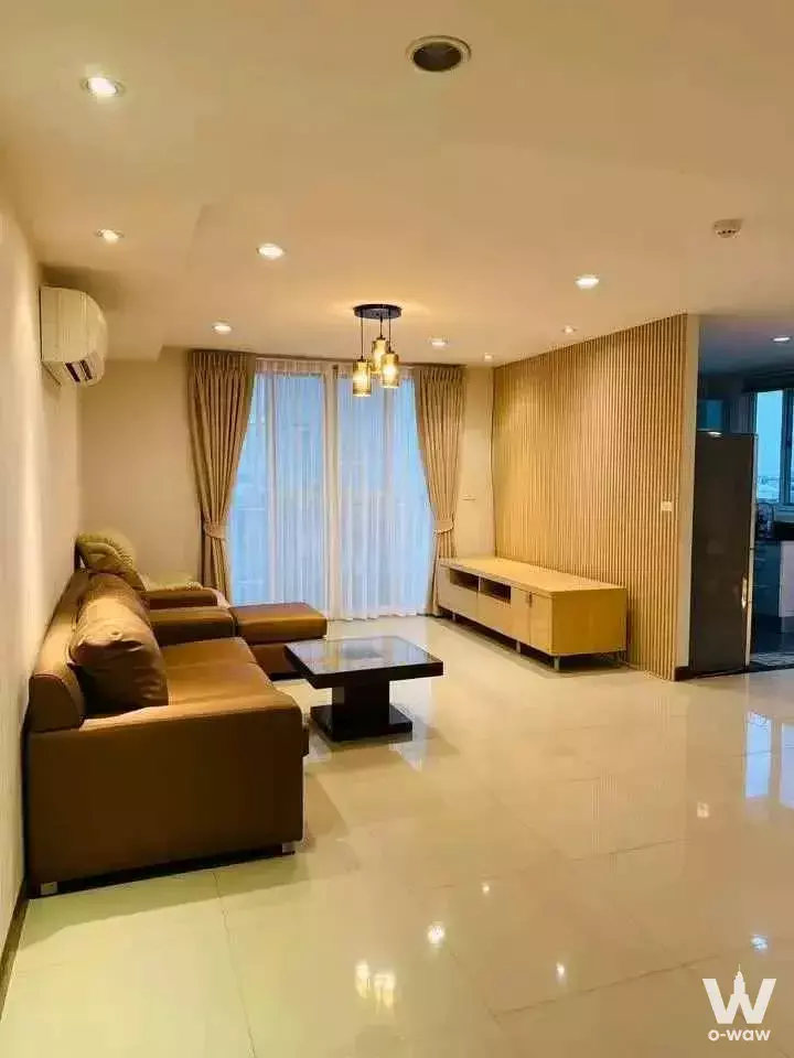 Modern living room with L-shaped brown leather sofa, wood slat accent wall, cream tile floors, and floor-to-ceiling windows