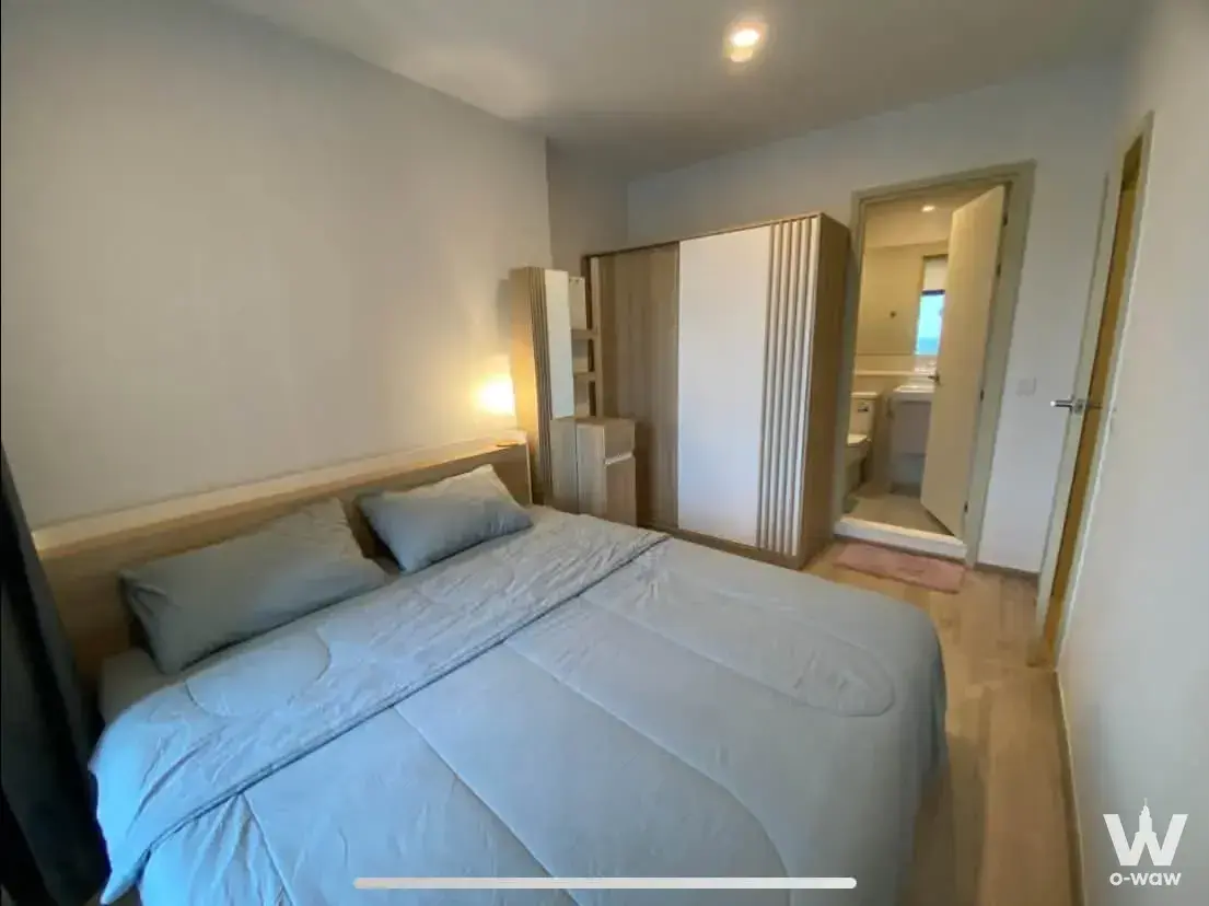 Life Rama 4 Asoke bedroom with blue-grey duvet, light wood shelving, and adjacent bathroom view