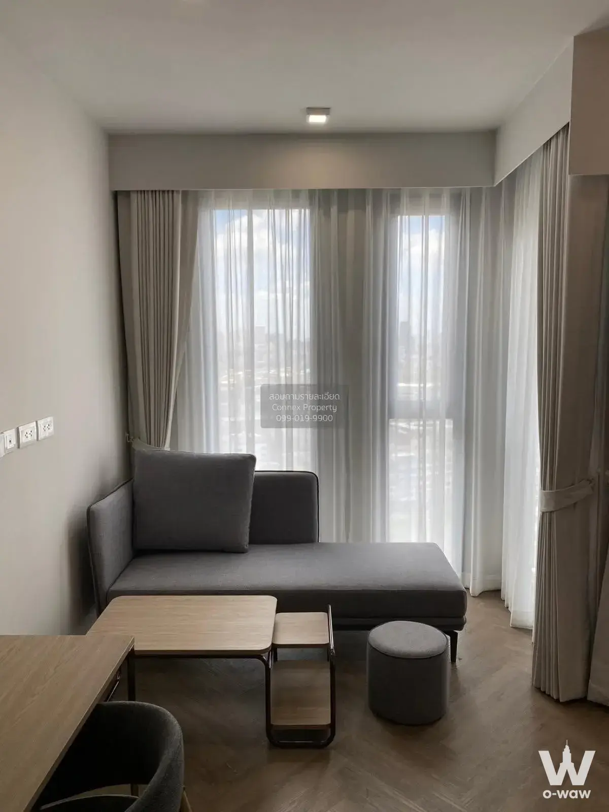 Grey chaise lounge on herringbone wood floor near sheer curtains in Chapter Chula-Samyan 1-bed condo for sale