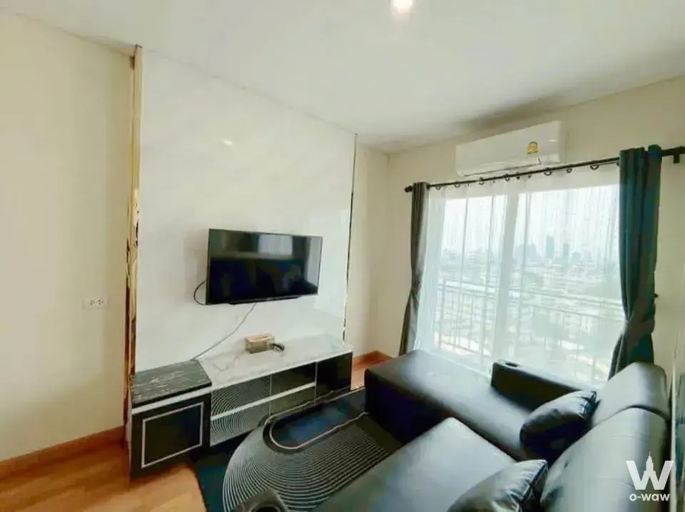 Living area in Lumpini Place Ratchada-Sathu showing a black leather sectional and city view through floor-to-ceiling windows