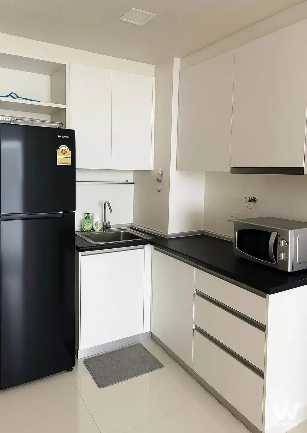 Compact kitchen with black countertop and white cabinets in Le Cote Sukhumvit 14 2-bed condo