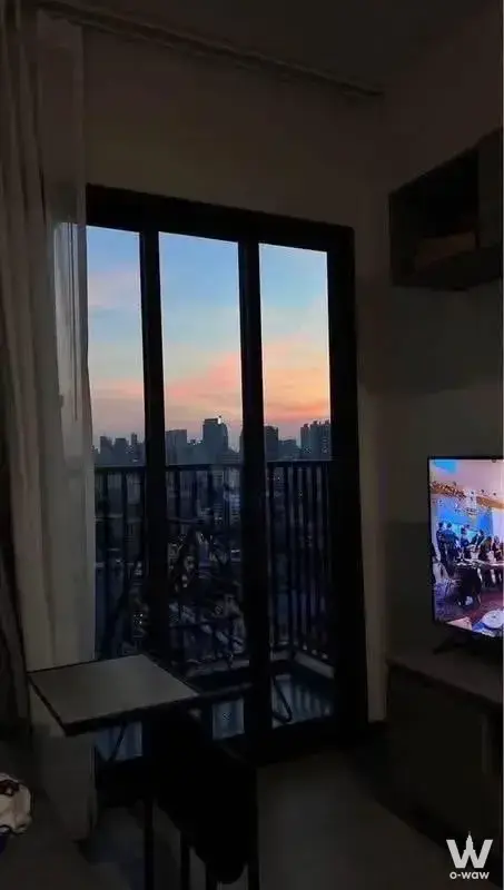 Living room with dusk city view through sliding doors in 1-bed unit for rent at THE BASE Phetchaburi-Thonglor