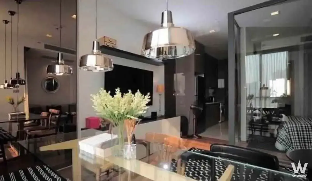 Open-plan living area with glass dining table, pendant lights, and mirrored wall in Hyde Sukhumvit 13