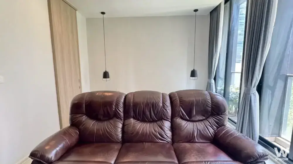Living room in a Noble Ploenchit rental featuring dark leather sofa and floor-to-ceiling windows