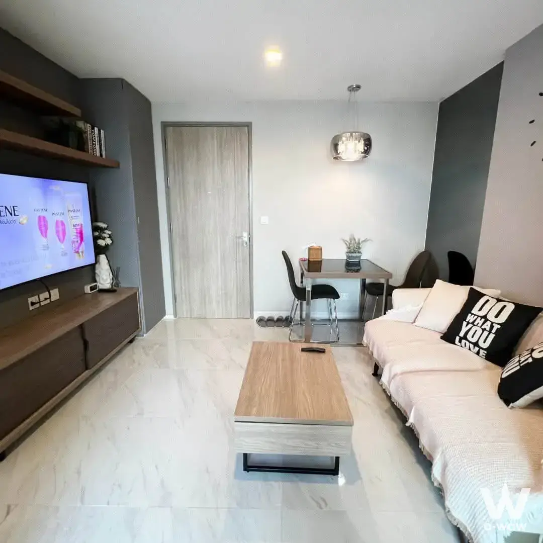 Living room in a 1-bed condo for sale at CHAMBERS CHAAN with beige sofa, dark wood console, and glass dining table