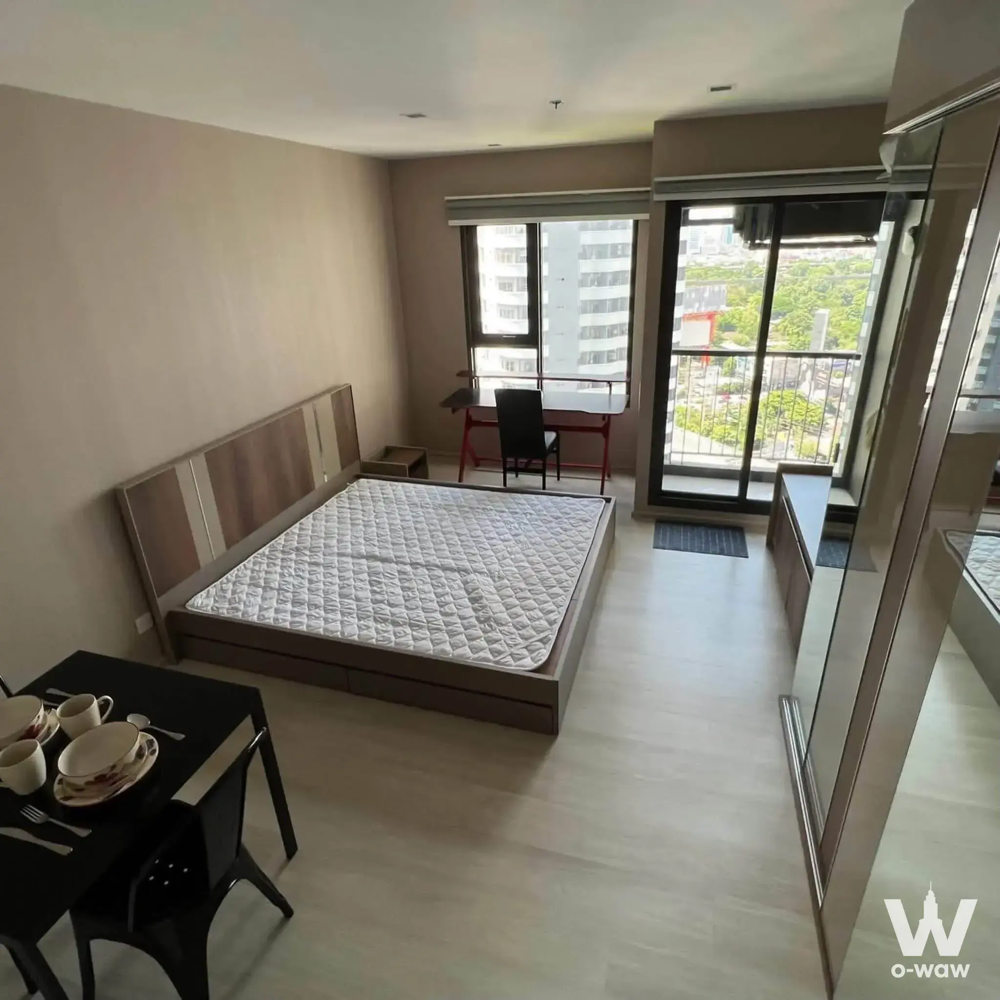 Modern studio with queen bed, black dining table, red desk, mirrored wardrobe, and balcony sliding doors