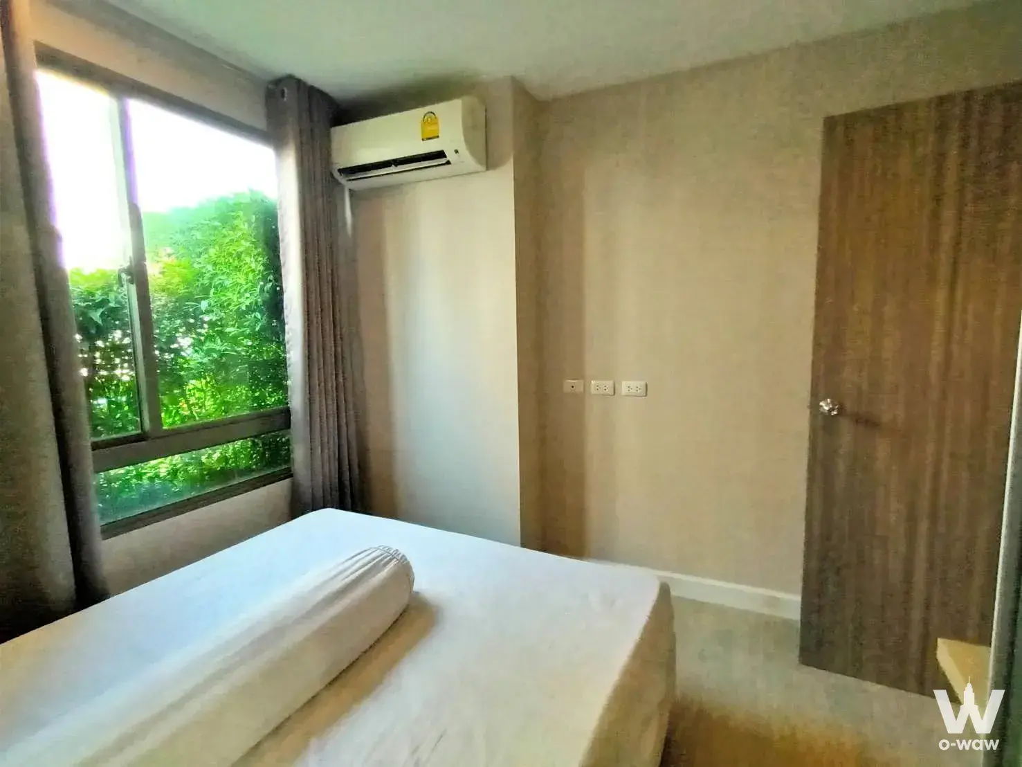 Minimalist bedroom with single bed, white linens, large window overlooking greenery, and wall-mounted AC in Metro Luxe