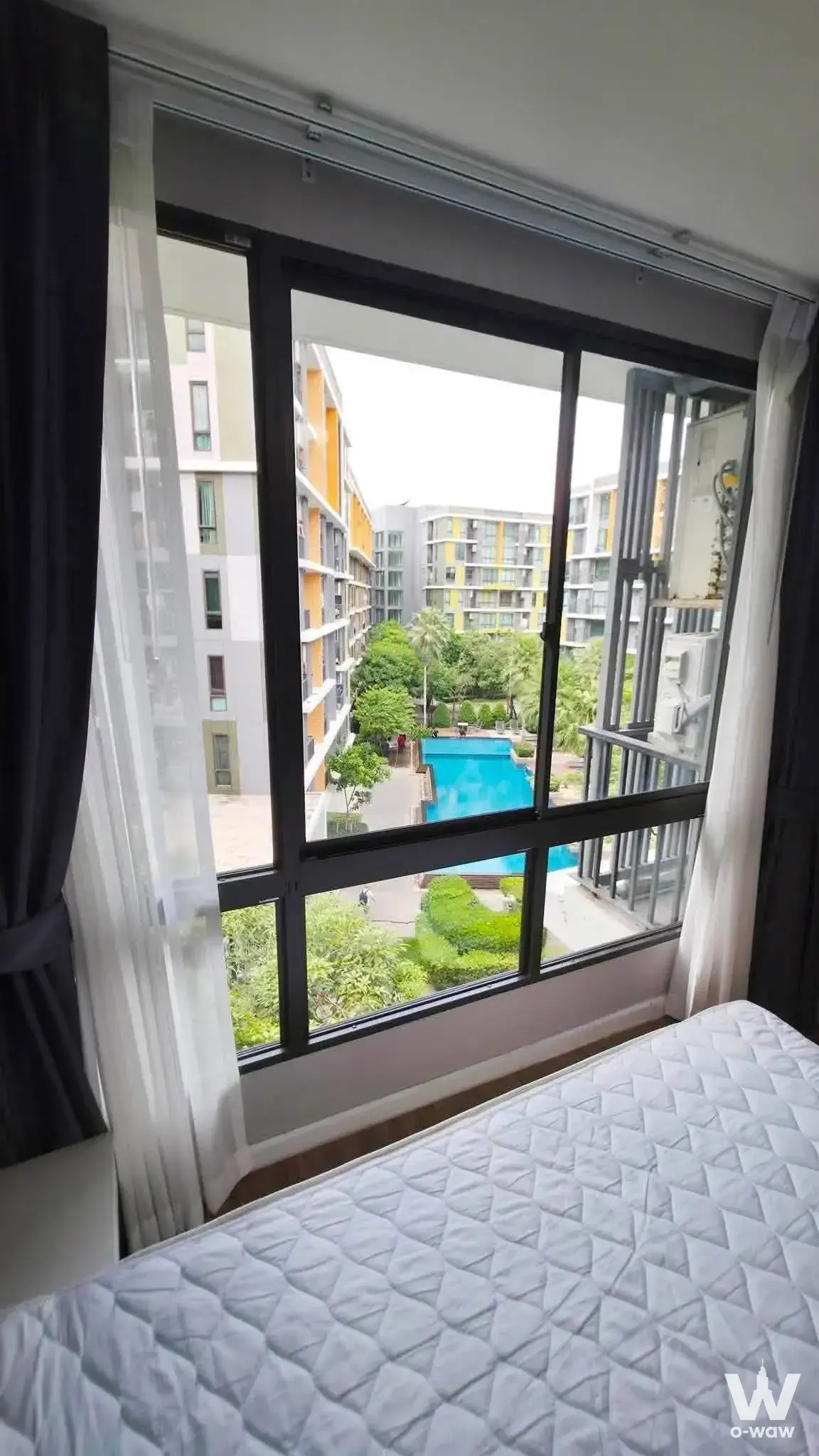 Bedroom in iCondo Sukhumvit 103 with floor-to-ceiling windows overlooking the pool courtyard