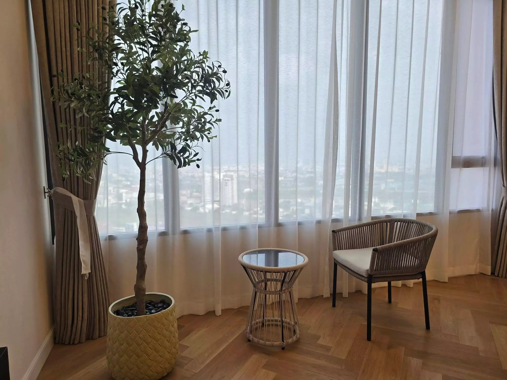 Bright living area in Landmark@MRTA 2-bed condo with herringbone floors, sheer curtains, and city skyline views