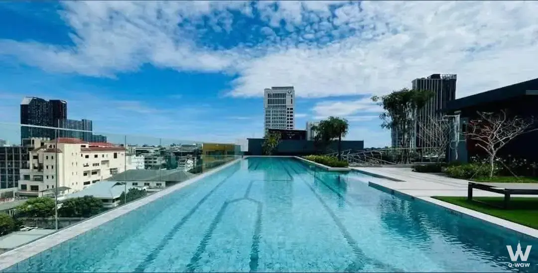Rooftop infinity pool at Plum Condo Sukhumvit 62 offering a long lap lane and panoramic city views under a bright blue sky