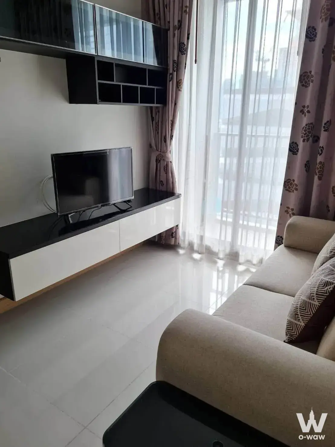 Furnished 1-bed condo in The President Condo Sukhumvit 81 showing a beige sofa, floating media console, and balcony access