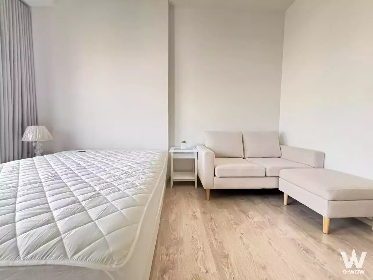 Minimalist studio with white walls, light wood floors, and beige sofa in The Tree Pattanakarn-Ekkamai