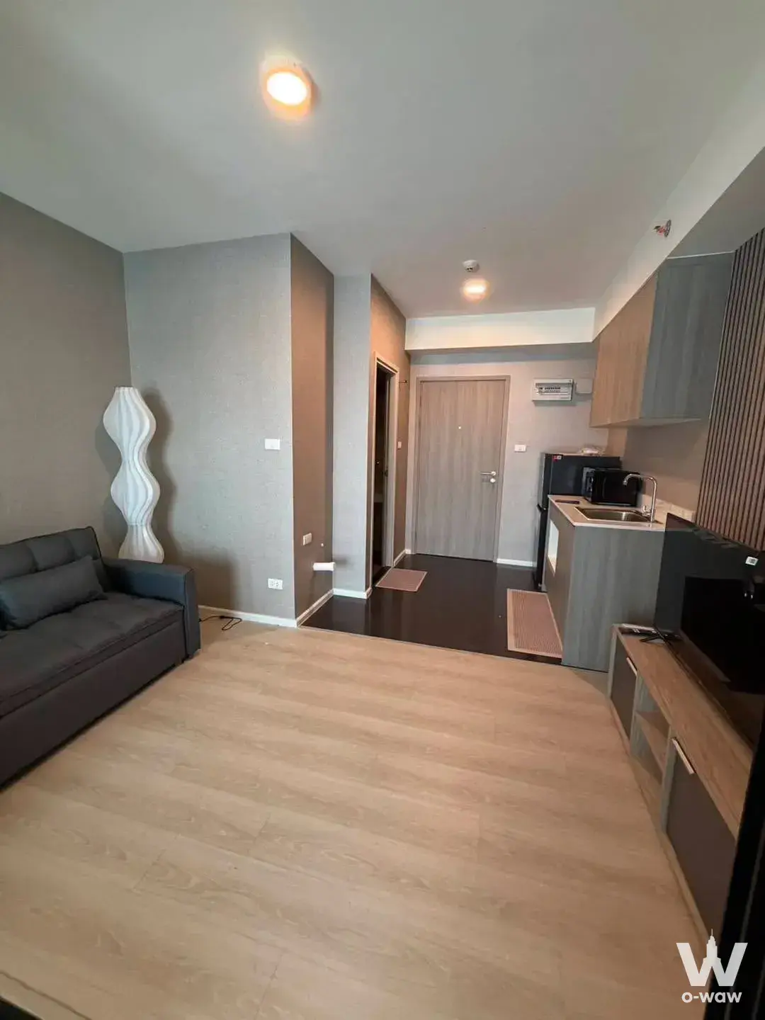Minimalist open-plan studio in A Space Condominium with oak flooring, grey walls, and compact kitchenette
