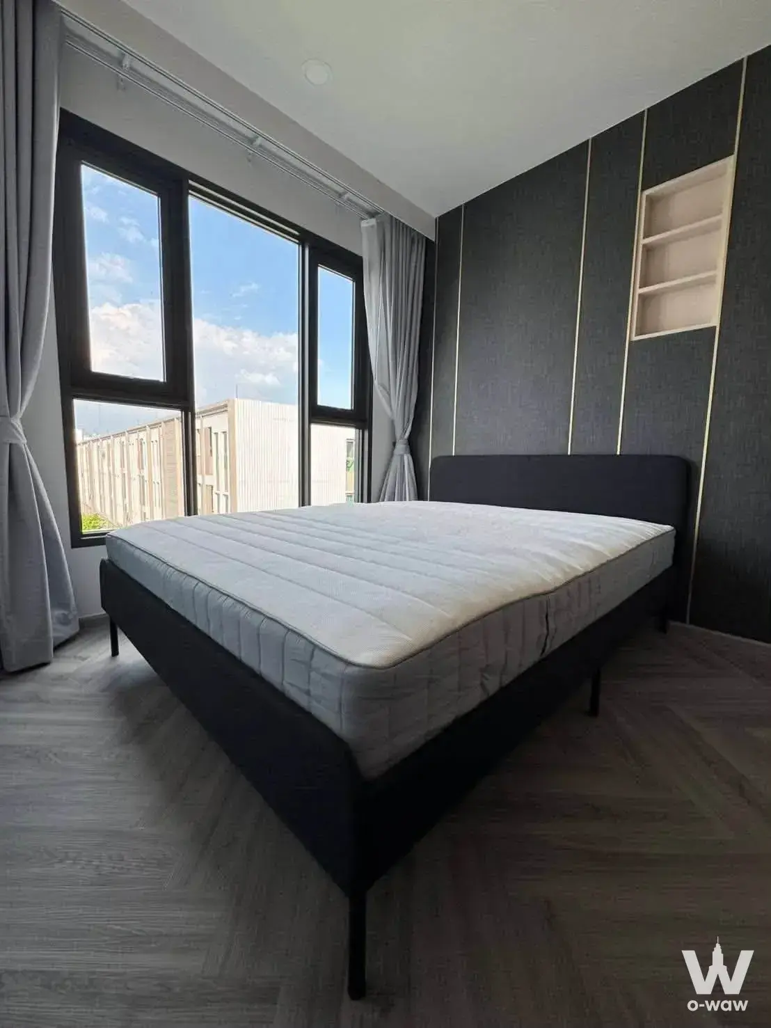 Aspire Arun Privé bedroom featuring a black upholstered bed, dark grey accent wall with gold trim, and large window view