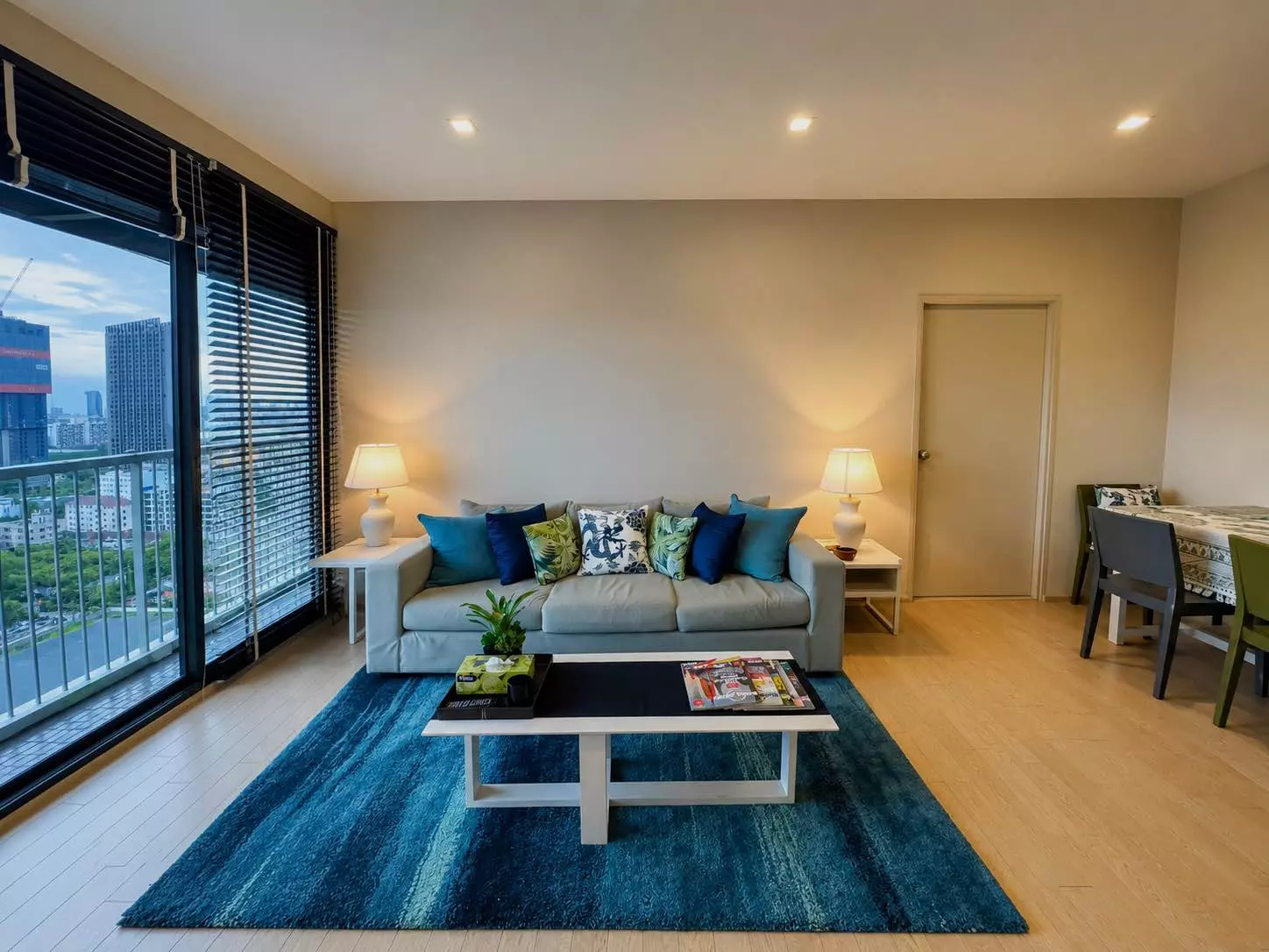 Living room in Noble Solo 1-bed condo with grey sofa, teal rug, and city view