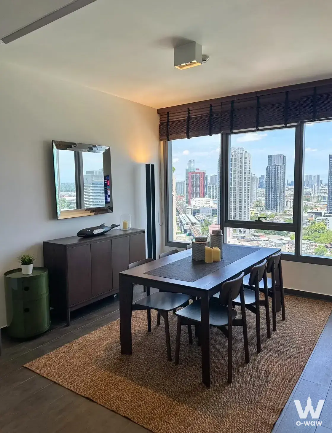 Dining room in The Lofts Ekkamai 2-bed condo with dark wood table, chairs, and city skyline view