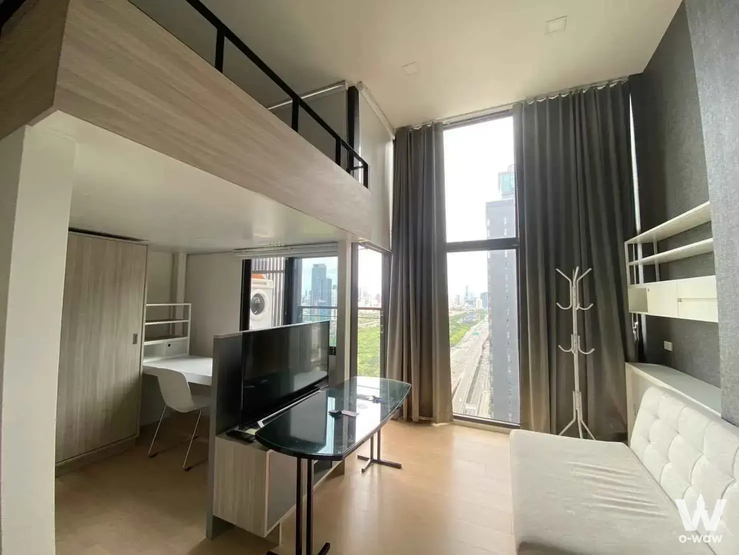 Studio apartment featuring mezzanine loft, grey sofa, and large window with city skyline view