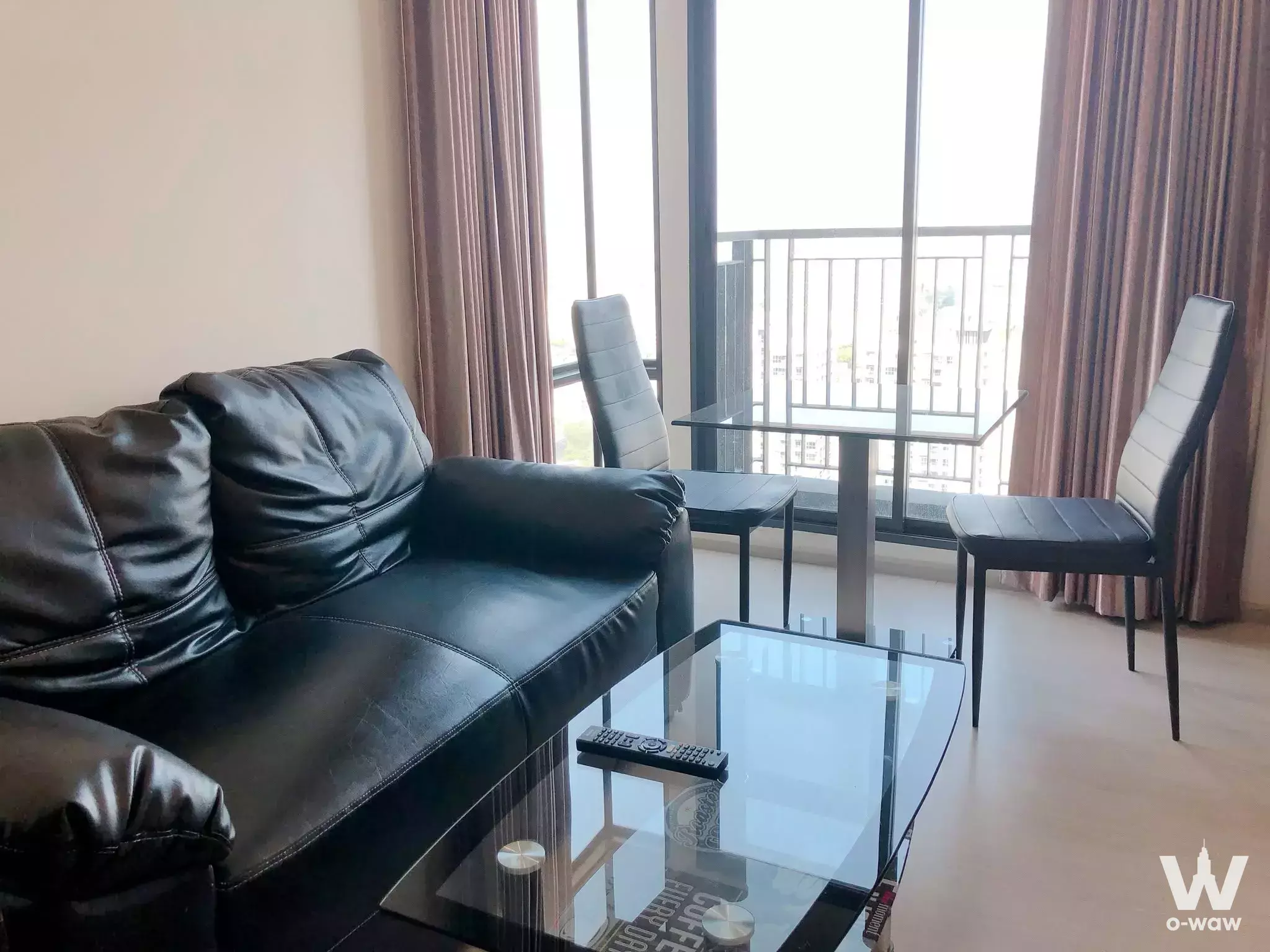 RHYTHM Asoke 2 2-bed condo living area with black leather sofa, glass dining set, and balcony city views