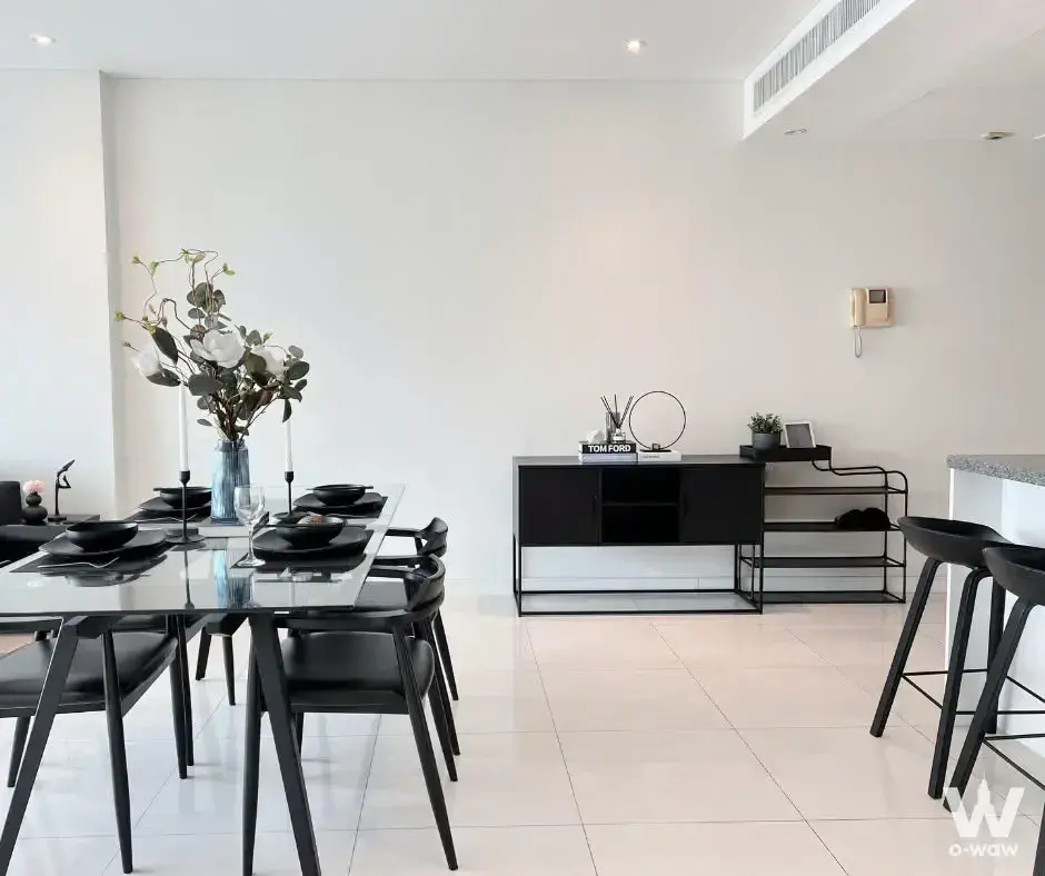 The dining room in this Fullerton Sukhumvit 2-bed rental has a glass table, black chairs and a kitchen island