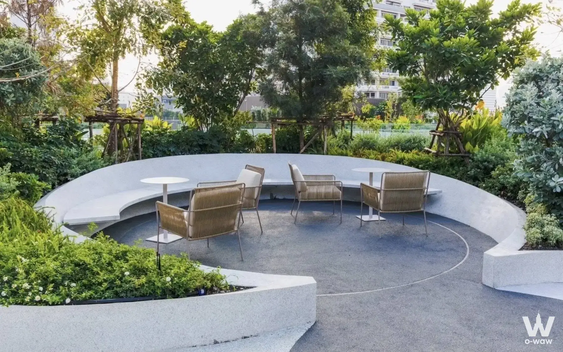 Rooftop garden lounge at Fynn Asoke with curved concrete benches, woven armchairs, and lush tropical greenery