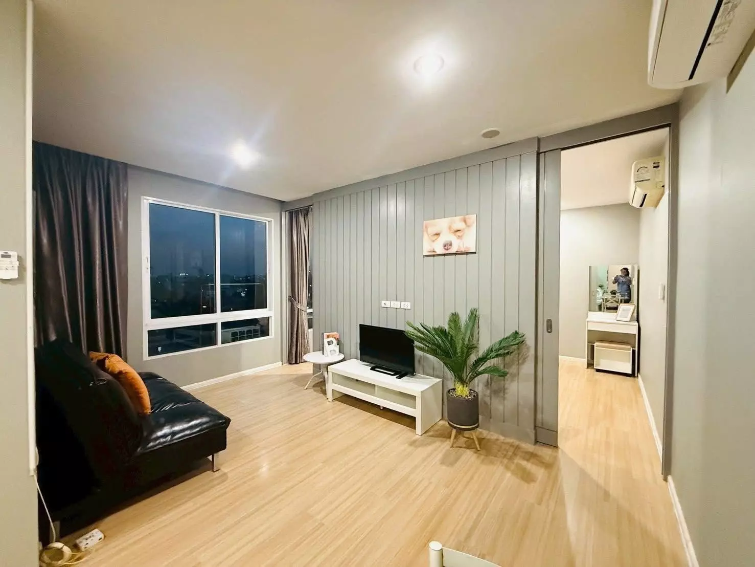 Living room with black leather sofa, orange pillows, and city view at Happy Condo Ladprao